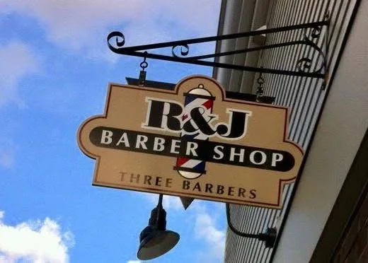 The R&J Barber Shop sign, with a barber pole and “Three Barbers”, hanging over the sidewalk